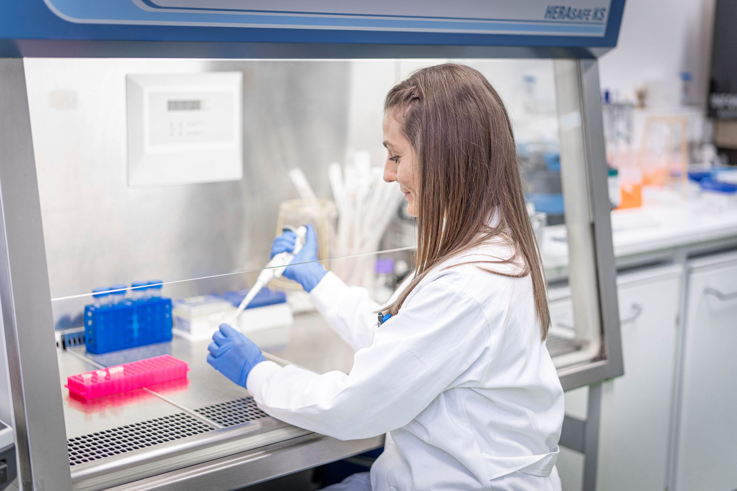 Female scientist smiling while working with pipette and other equipment.