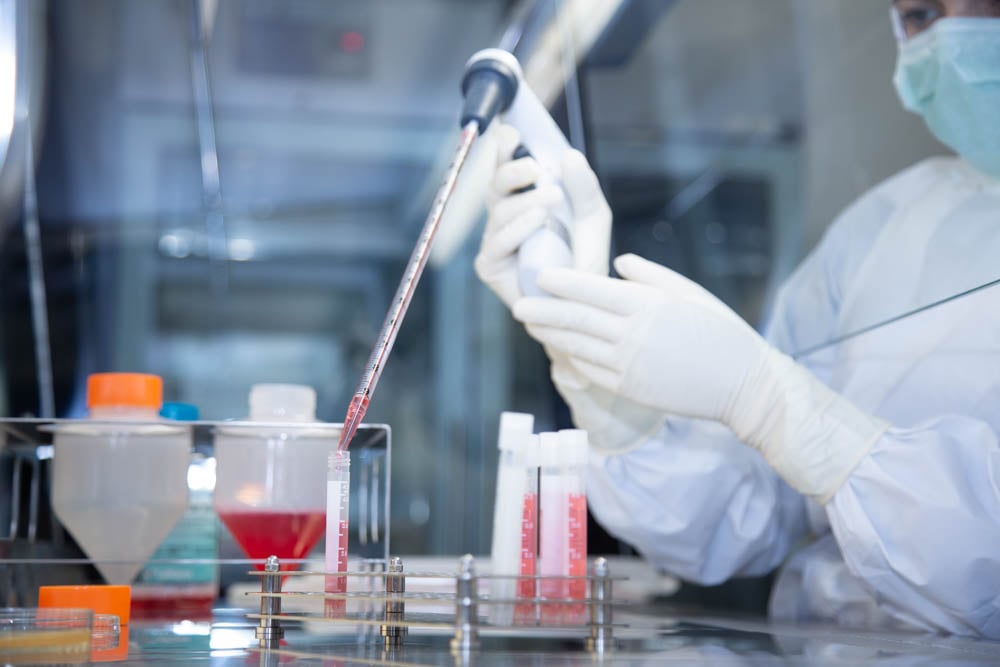 Close-up of cells being worked with in controlled environment under a hood by a scientist in PPE.